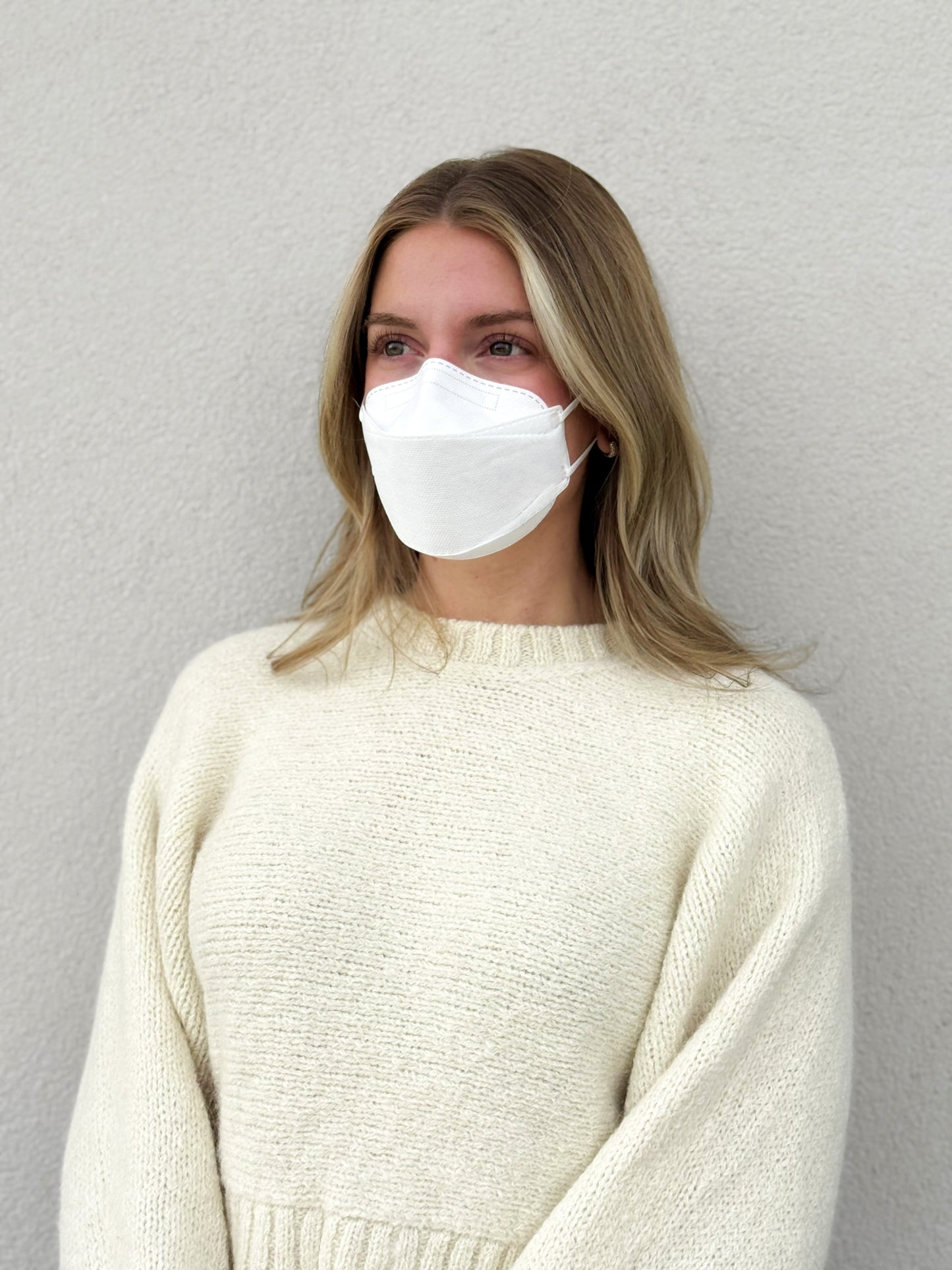 Side view of woman wearing medium white KN95 earloop respirator style trifold face mask breatheTeq USA made in Canada